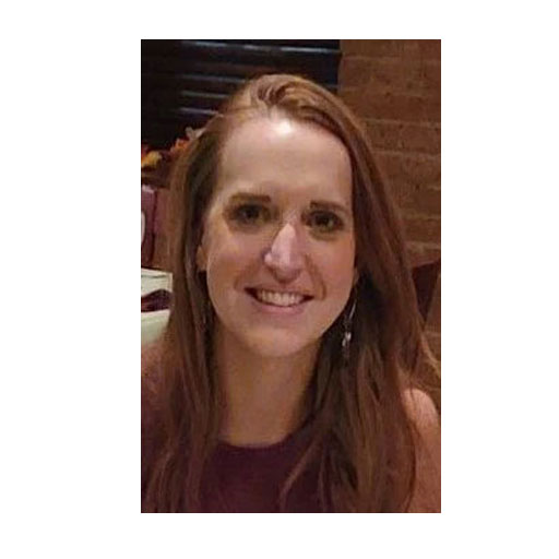 Village of Painted Post Trustee/Police Department Britany Elsey with long reddish brown hair and a dark sleeveless blouse on, sitting in front of a brick wall