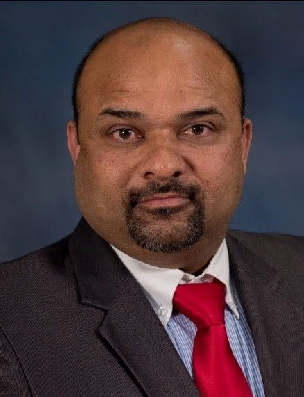 Village of Painted Post Trustee/Fire Department Venu Yama in a dark suit with a white collar and red tie and blue background